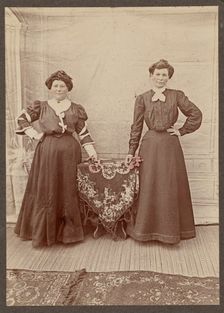 Two women standing at a table holding flowers, about 1875. Creator: Unknown