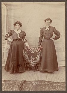 Two women standing at a table holding flowers, about 1875. Creator: Unknown