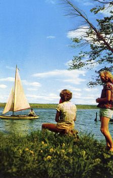 Two women watching a sailing boat on a lake, Michigan Water Wonderland, USA, 1955