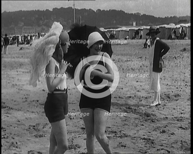 Two Young Female Civilians Wearing Swimsuits Holding Feathered Parasols on a Beach, 1920. Creator: British Pathe Ltd.