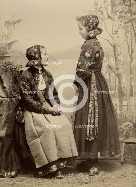 Two young girls pose in costumes from Dala-Floda with floral jackets and hats, 1890-1900. Creator: Helene Edlund.