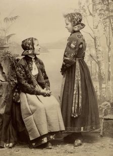 Two young girls pose in costumes from Dala-Floda with floral jackets and hats, 1890-1900. Creator: Helene Edlund