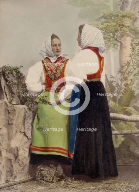 Two young women pose in folk costumes, with dotted headdresses, 1886-1890. Creator: Helene Edlund.