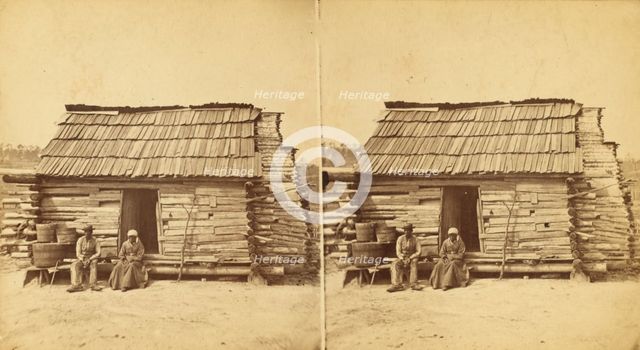Uncle Ben's cabin, [Elderly couple sitting in front of a cabin], (1868-1900?). Creator: Unknown.