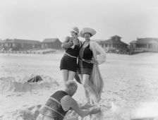 Unidentified man building sand castle and two women, Long Beach, New York, between 1911 and 1942. Creator: Arnold Genthe