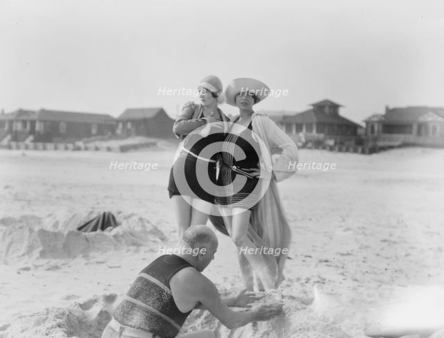Unidentified man building sand castle and two women, Long Beach, New York, between 1911 and 1942. Creator: Arnold Genthe.