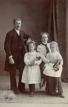Unidentified family with two girls holding dolls. Creator: Priyalalls Photography