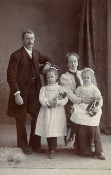 Unidentified family with two girls holding dolls. Creator: Priyalalls Photography