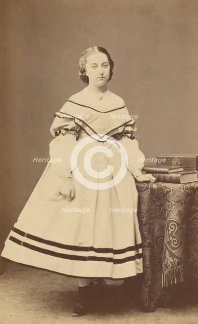 Unidentified woman standing near a table with books on top, 1865-1875. Creator: Bayard & Bertall.