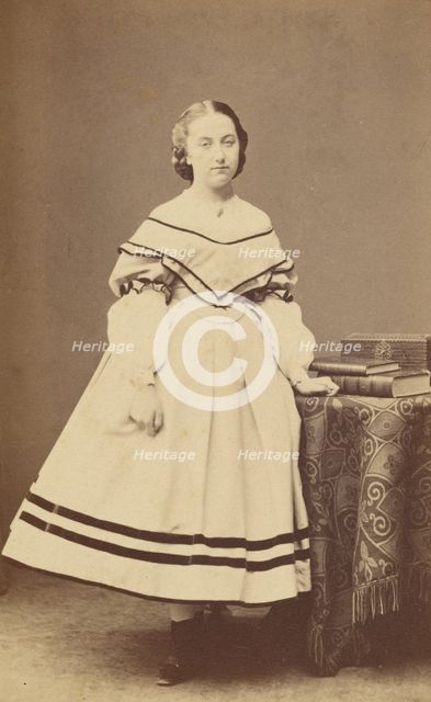 Unidentified woman standing near a table with books on top, 1865-1875. Creator: Bayard & Bertall.