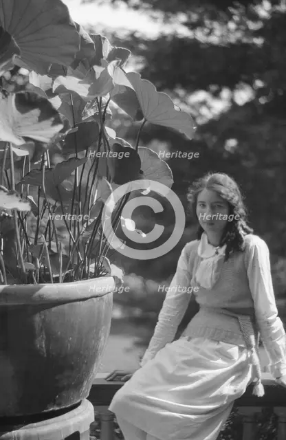 Unidentified woman seated in a garden next to a large potted plant, between 1917 and 1934. Creator: Arnold Genthe.