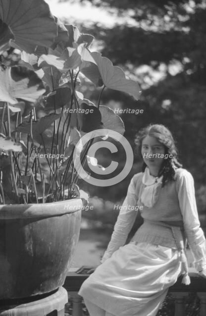Unidentified woman seated in a garden next to a large potted plant, between 1917 and 1934. Creator: Arnold Genthe.