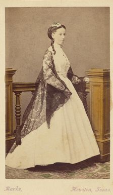 Unidentified woman wearing a white dress and black shawl, standing, 1870-1875. Creator: H. R. Marks