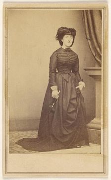 Unidentified woman wearing a hat and long dark dress, about 1868. Creator: Mathew Brady