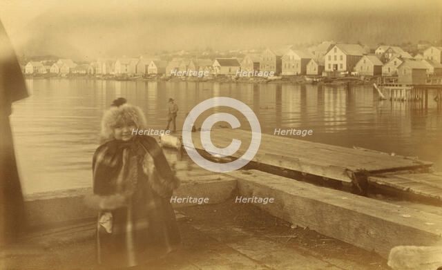Unidentified young girl standing on wharf, with buildings along waterfront...,1894 or 1895. Creator: Alfred Lee Broadbent.