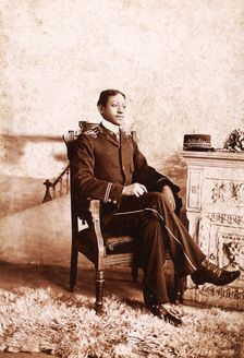 Uniformed man seated, on the mantlepiece is his cap, embroidered with the name...., c1900-c1909. Creator: Roche