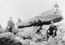Unknown men and boy, unknown location posing on large rocks, c1900s. Creator: Robert Augustus Henry L'Estrange