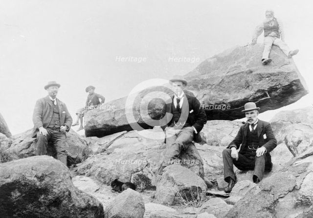 Unknown men and boy, unknown location posing on large rocks, c1900s. Creator: Robert Augustus Henry L'Estrange.