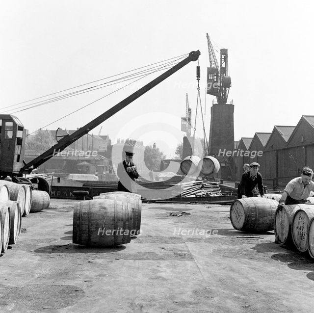 Unloading wine barrels, London Docks, 1953. Creator: Henry Grant.
