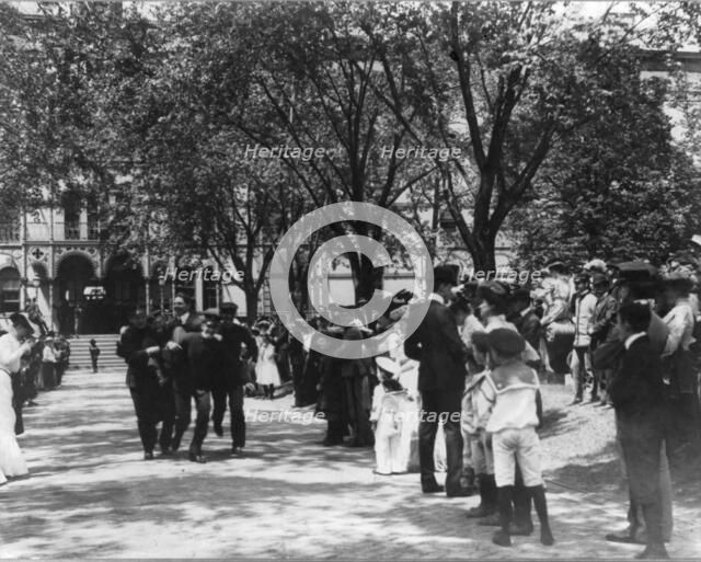 U.S. Naval Academy, Annapolis: 4 midshipmen carrying a man; crowd of guests along sidewalk, (1902?). Creator: Frances Benjamin Johnston.