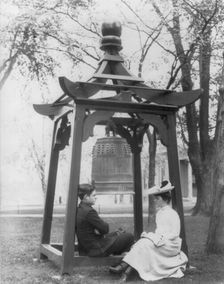 U.S. Naval Academy, Annapolis, Md. 1902?: midshipman and girl sitting beneath bell, (1902?). Creator: Frances Benjamin Johnston