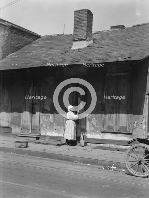 View from across street of a woman with a broom standing in a doorway, New Orleans, c1920-c1926. Creator: Arnold Genthe.