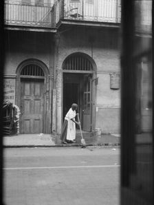 View from across street of a woman cleaning the sidewalk, New Orleans, between 1920 and 1926. Creator: Arnold Genthe