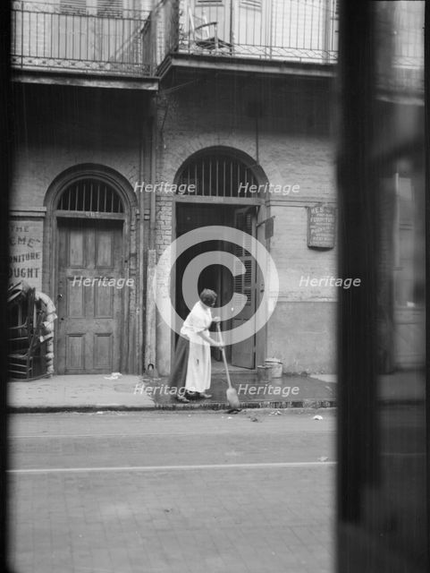 View from across street of a woman cleaning the sidewalk, New Orleans, between 1920 and 1926. Creator: Arnold Genthe.