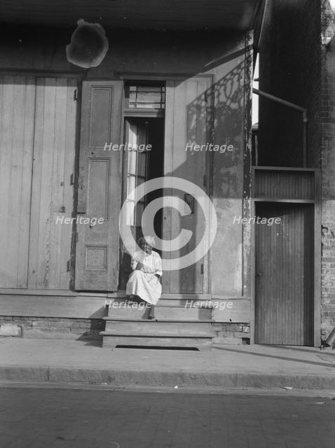 View from across street of a woman sitting on steps, New Orleans, between 1920 and 1926. Creator: Arnold Genthe.