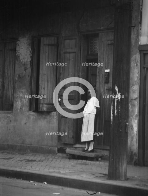 View from across street of a woman standing in a doorway in the French Quarter, New..., c1920-c1926. Creator: Arnold Genthe.