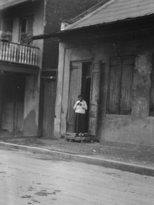 View from across street of a woman standing in a doorway in the French Quarter, New..., c1920-c1926. Creator: Arnold Genthe