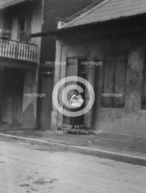 View from across street of a woman standing in a doorway in the French Quarter, New..., c1920-c1926. Creator: Arnold Genthe.