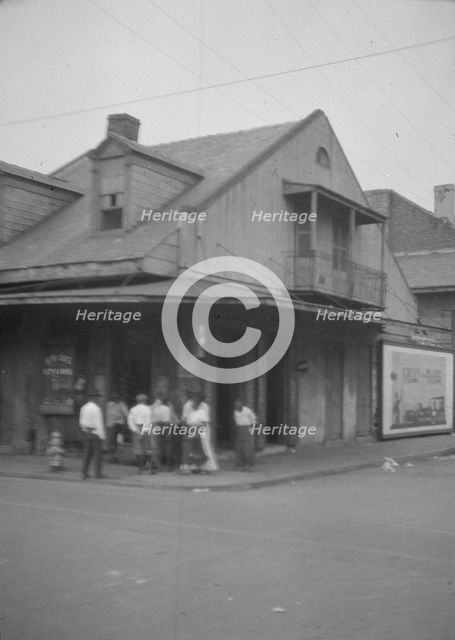 View from across street of a group of men on a street corner, New Orleans, between 1920 and 1926. Creator: Arnold Genthe.