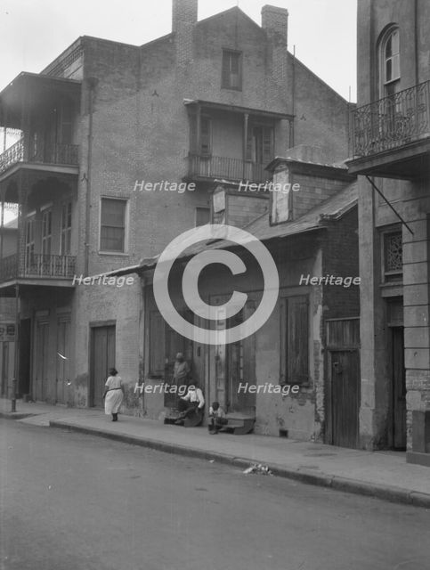 View from across street of a man and child sitting on steps and a woman walking down..., c1920-1926. Creator: Arnold Genthe.