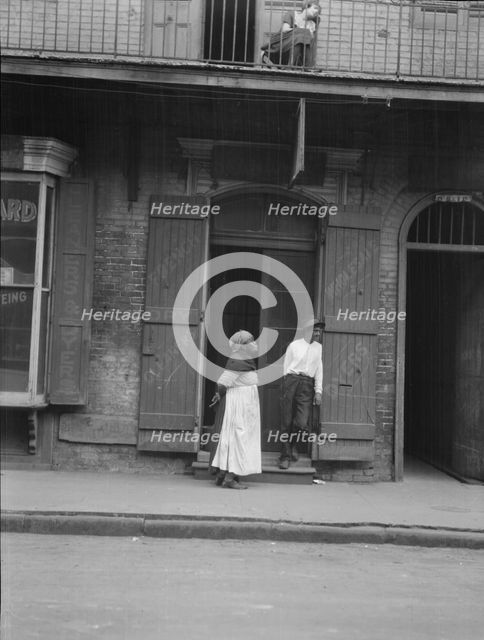 View from across street of a man and woman standing by a doorway and a woman seated...c1920-1926. Creator: Arnold Genthe.