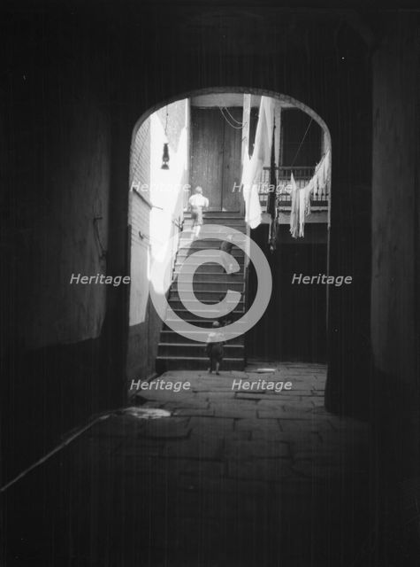 View of a courtyard through an arched passageway, New Orleans, between 1920 and 1926. Creator: Arnold Genthe.