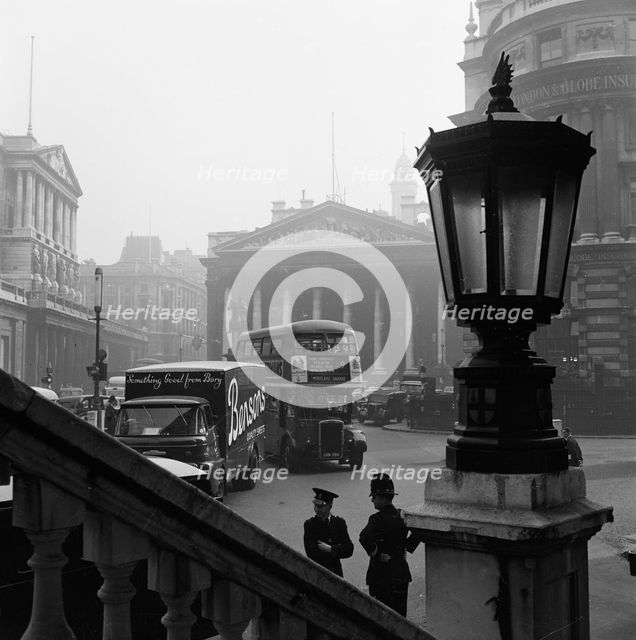 View past a lamp showing the busy traffic outside The Bank of England..., London, probably 1960s. Creator: John Gay.