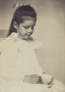 Young girl in white dress, seated holding teacup and saucer, c1900. Creator: Anne K Pilsbury