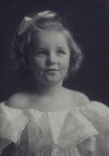 Young girl in a white off-the-shoulder dress with a ribbon in her hair , c1900. Creator: Anne K Pilsbury