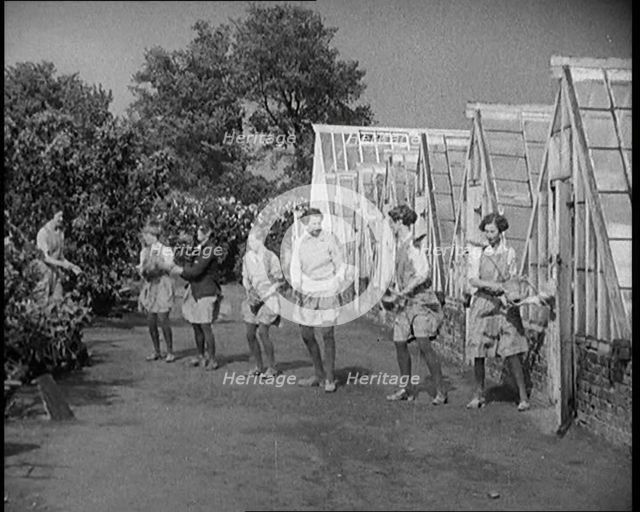 Young Female Civilians Outside a Greenhouse Standing in a Row Passing Plant Pots Along..., 1920. Creator: British Pathe Ltd.