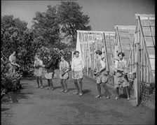 Young Female Civilians Outside a Greenhouse Standing in a Row Passing Plant Pots Along..., 1920. Creator: British Pathe Ltd