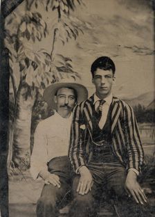 Young Man in a Striped Jacket, Sitting on the Lap of Another Man in Front of Painted..., 1860s-80s. Creator: Unknown
