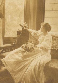 Young woman seated by a window with flowers in her lap, c1900. Creator: Mary A. Bartlett
